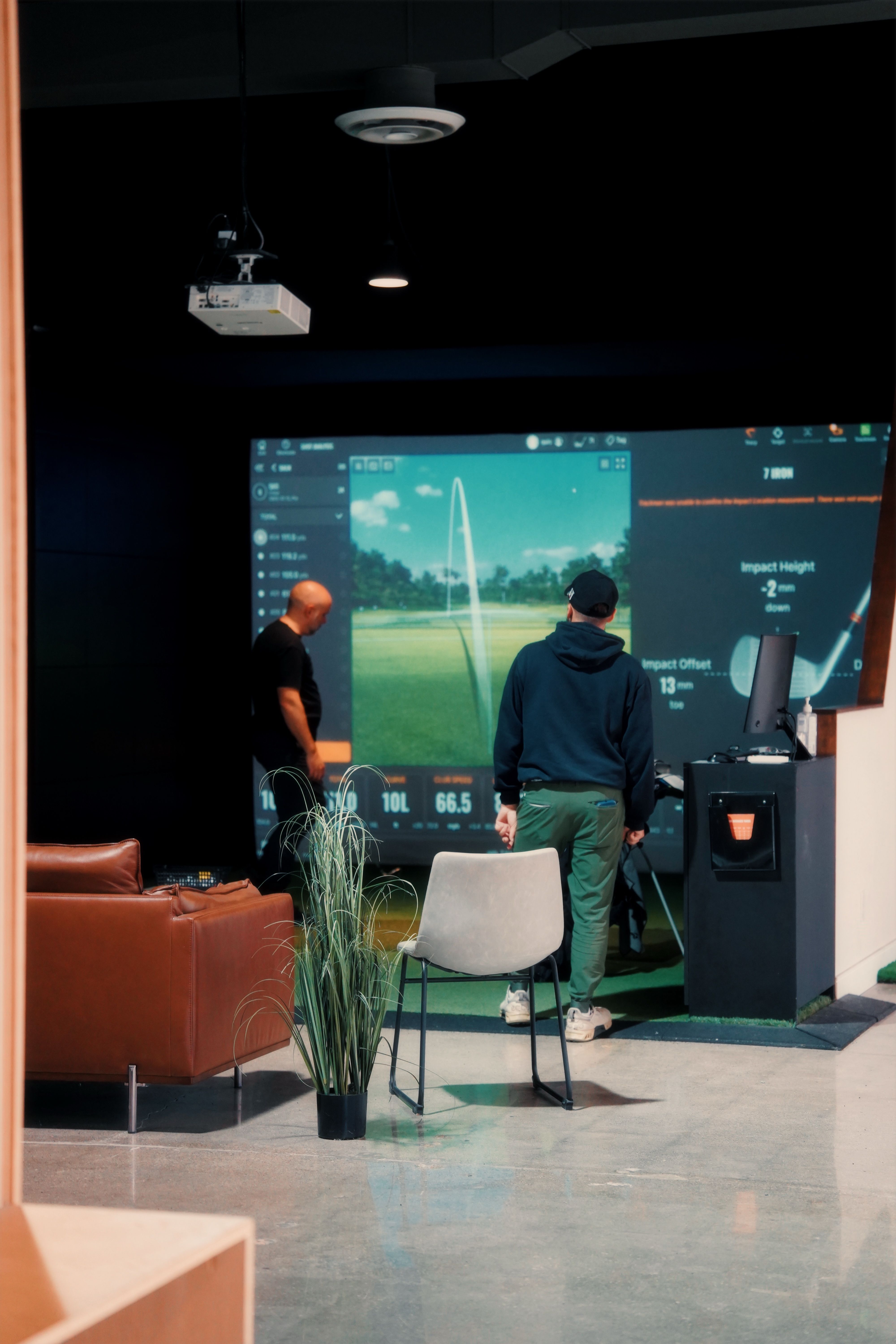 Two players watching ball-flight data on a bay screen in a darkened room.